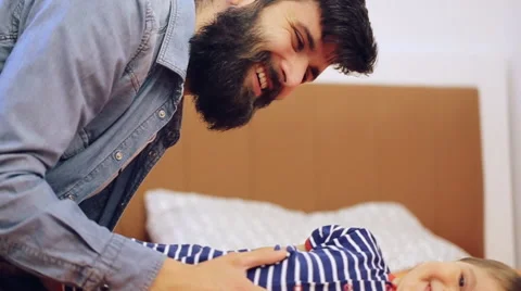 Little smiling boy lying on bed playing with his bearded father Stock Footage 64521415