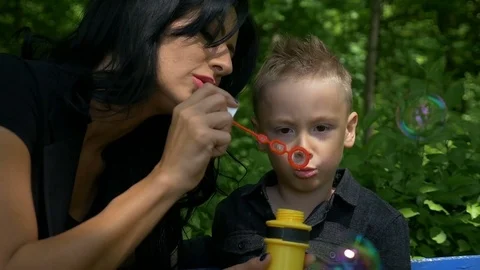 Little son blowing soap bubbles in the sunlight with his young mother at the  Stock Footage 76643581