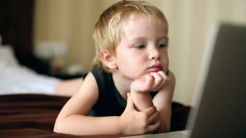 Little sweet blonde boy using modern laptop inside resting on bed. Early 스톡 동영상 138881709