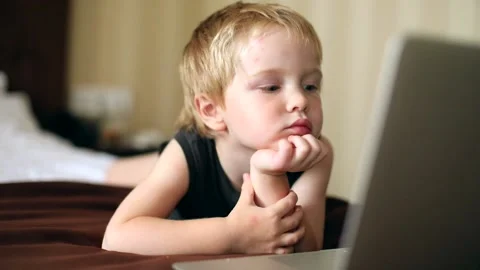 Little thoughtful boy using notebook laptop indoor resting on bed. Early educati 스톡 동영상 138982772