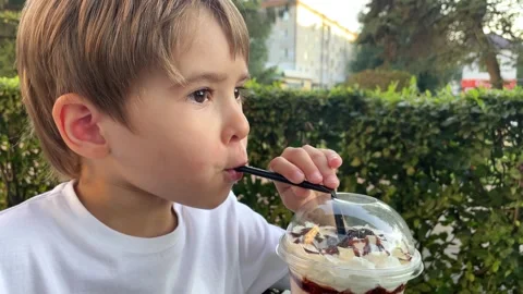 Little toddler boy drinks a milkshake through a straw on the terrace. Cafe Stock Footage 246722632