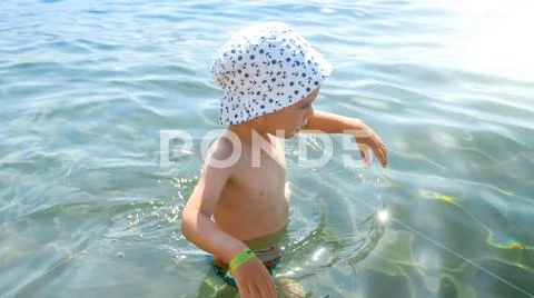 Little toddler boy wearing hat walking in sea at hot sunny day Stock Photos