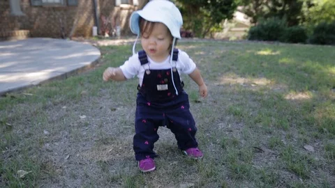 Little Toddler Trying to Jump while Playing Outside in Overalls Stock Footage 94076934