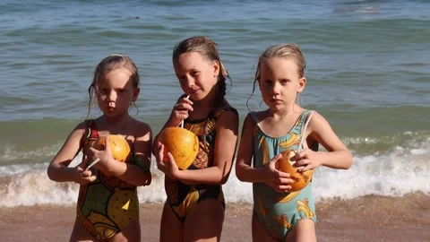 Little triplet sisters drinking coconuts on the beach 库存影片 323735341