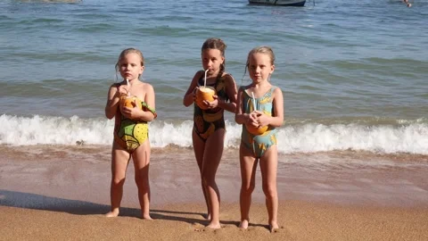 Little triplet sisters drinking coconuts on the beach 库存影片 323736505