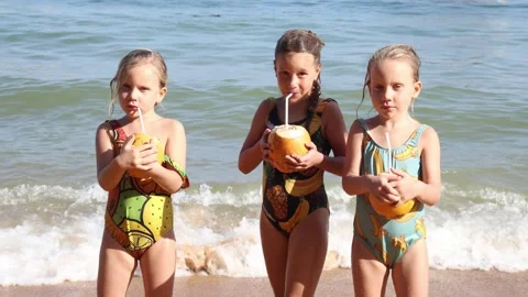 Little triplet sisters drinking coconuts on the beach 库存影片 323744648