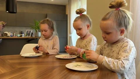 Little triplet sisters peeling Easter eggs at the dinner table on Easter 库存影片 281596780