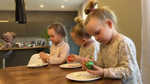 Little triplet sisters peeling Easter eggs at the dinner table on Easter Stockbeeldmateriaal 281596811