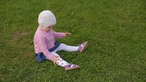 Little two-year-old beautiful girl in a hat sits on the green grass on a summer Stock Footage 75763083