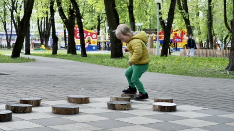 Little Two-Year-Old Boy Plays Big Checkers in Green Pants and Yellow Jacket Stock Footage 241322488