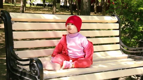 Little two year old child is sitting on the bench and knocks on the legs. spring Stock Footage 90265121