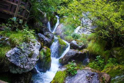 Little waterfall surrounded by huge rocks in the river flow in the forest, Italy Stock Photos