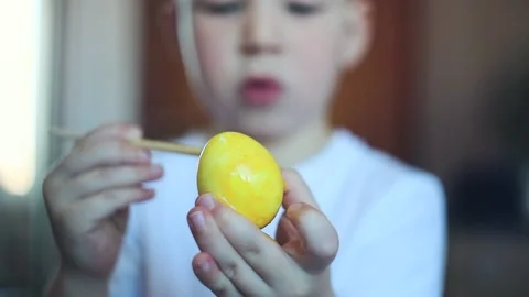 A little white-skinned boy with a diligent face paints an Easter egg.  Easter Eg Stock Footage 150034682