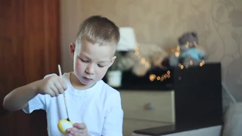 A little white-skinned boy with a diligent face paints an Easter egg.  Easter Eg Stock Footage 150034684