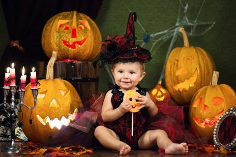 Little witch laughs with candy in the hands among the pumpkins and candles. Stock Photos