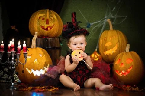 Little witch laughs with candy in the hands among the pumpkins and candles. Stock Photos