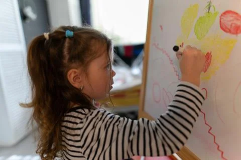 Little young girl draws with multi-colored felt-tip pens on the blackboard. Stock Photos