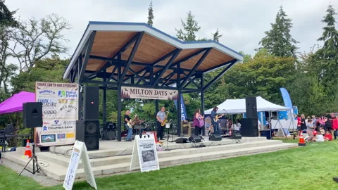 A live band performs on an outdoor stage under a wooden pavilion during a com-55 Stock-Footage 344605419
