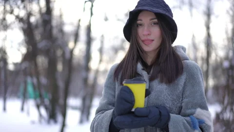 Live camera zoom in to beautiful slim young woman drinking coffee in winter park Video stock 219905530