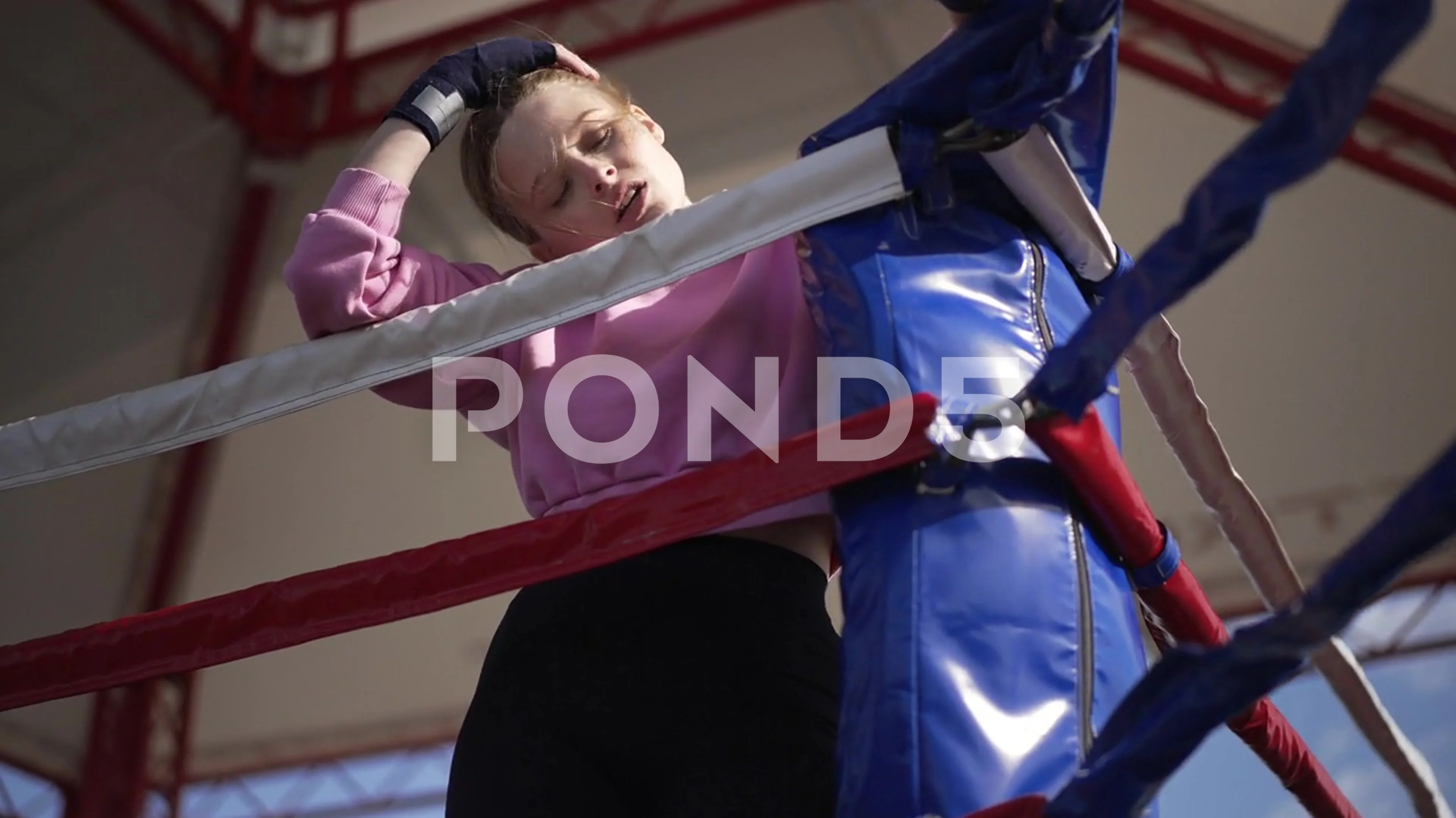 Live camera zoom in to exhausted female boxer leaning on boxing ropes  breathing