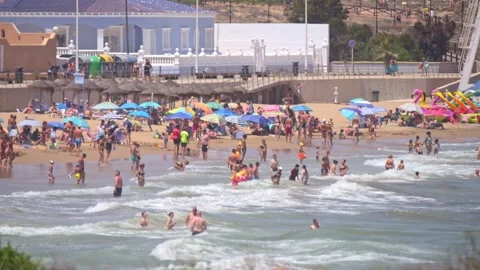 A lively beach scene unfolds, packed with vacationers and colorful umbrella.. Stock Footage 249591373