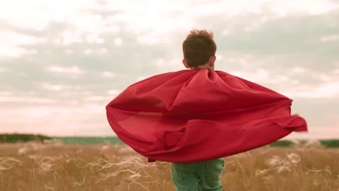 Lively boy runs across field of growing plants with red cape fluttering in wind Stock Footage 255613161