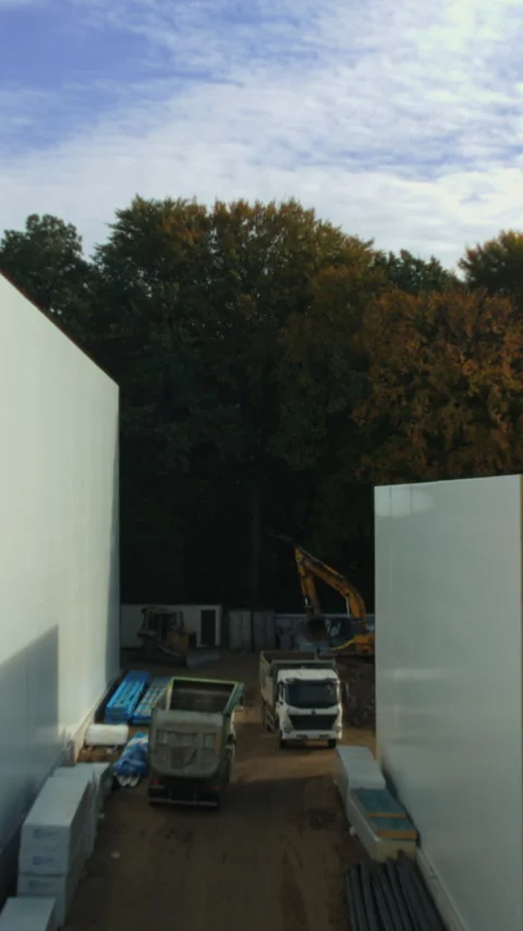 A lively construction site with trucks, white walls, and trees Stock Footage 319614868