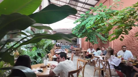 Lively Courtyard Restaurant Interior with Patrons Dining and Open Kitchen in Stock Footage 337137791