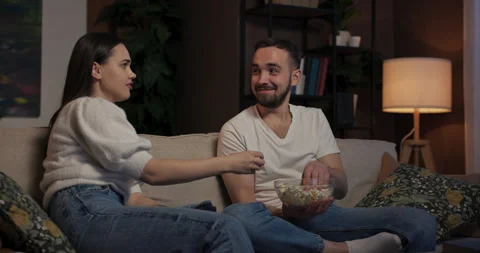 Lliving room only source of light coming from TV screen young woman and man sit Stock Footage 263613198