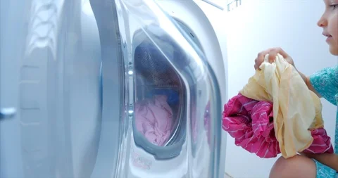 Load clothes to the washing machine. Little Girl Loads the Laundry in the Stock Footage 106366249