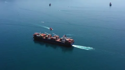 Loaded container cargo vessel traveling being assisted by tugboat docking on Stock Footage 336445890