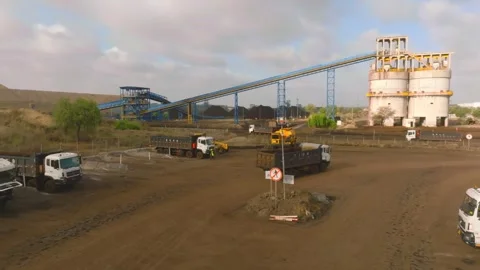 Loaded dump trucks move through Thar Engro Coal Mine Block II beside conveyors Stock-Footage 344055917