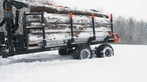 A loaded tractor with a trailer of logs is trying to leave a snow-covered field Stock Footage 169549092