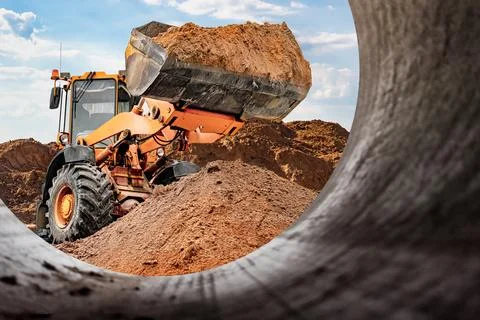 A loader is actively moving dirt at a construction site where new pipes are b Photos