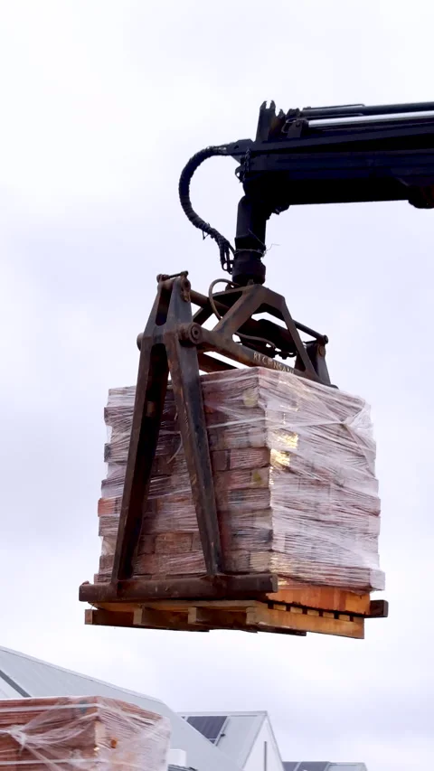 Loader crane use brick grab to lift pallet full of bricks off transport truck Stock Footage 342577712