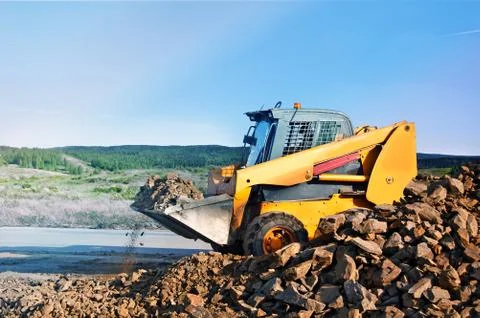 Loader dumping stone on road on the natural background In the countryside. Stock Photos