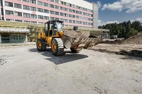A loader lifts soil from the ground at a construction site in a city. The mac Stock Photos