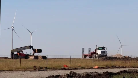 Loader loading a flatbed trailer near Kansas wind turbines Stock Footage 347405193