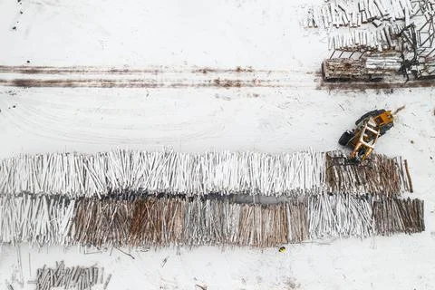 Loader loads logs stacked in piles covered with snow top view Stock Photos