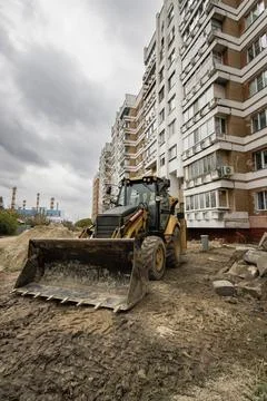 A loader machine is working on the ground near a residential building in an u 库存照片