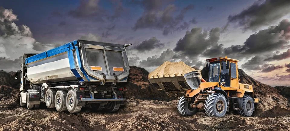 A loader or bedozer loads a dump truck car with sand at a construction site.  Stock Photos