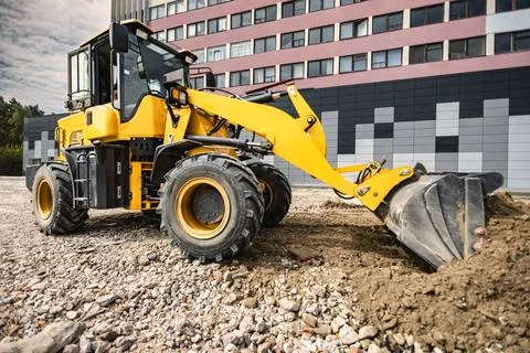 Loader is seen working on a construction site, pushing dirt and gravel. The m Stock Photos