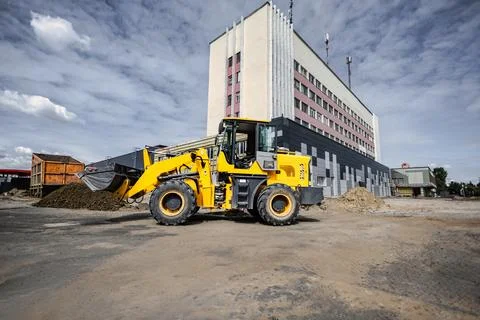 A loader is working at a construction site near a large building, moving dirt Stock Photos
