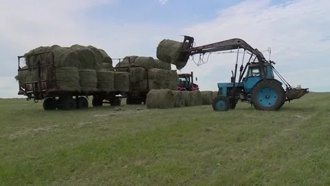 Loading bales of hay Tractor to the flatbed trailer in the field. countryside Stock Footage 132737339