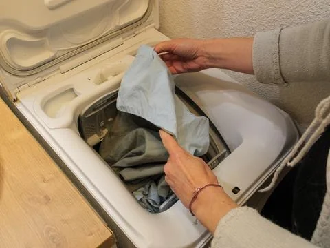 Loading clothes into a top loading washing machine at home Stock Photos