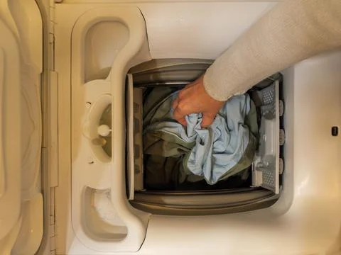 Loading clothes into a top-loading washing machine at home Stock Photos
