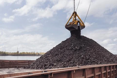 Loading coal using a floating crane onto a barge. Coal is poured from a bucket Stock Photos