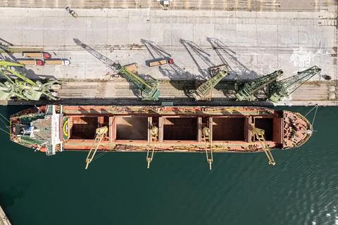 Loading dry cargo ship of wheat by cranes in port. Top down view loading in.. Stock Photos