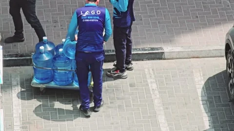Loading large blue water bottles on a hand truck, likely for an office or home 스톡 동영상 311891864