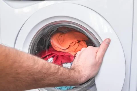 Loading laundry in the washing machine. A man's hand opens the door of the wa 库存照片